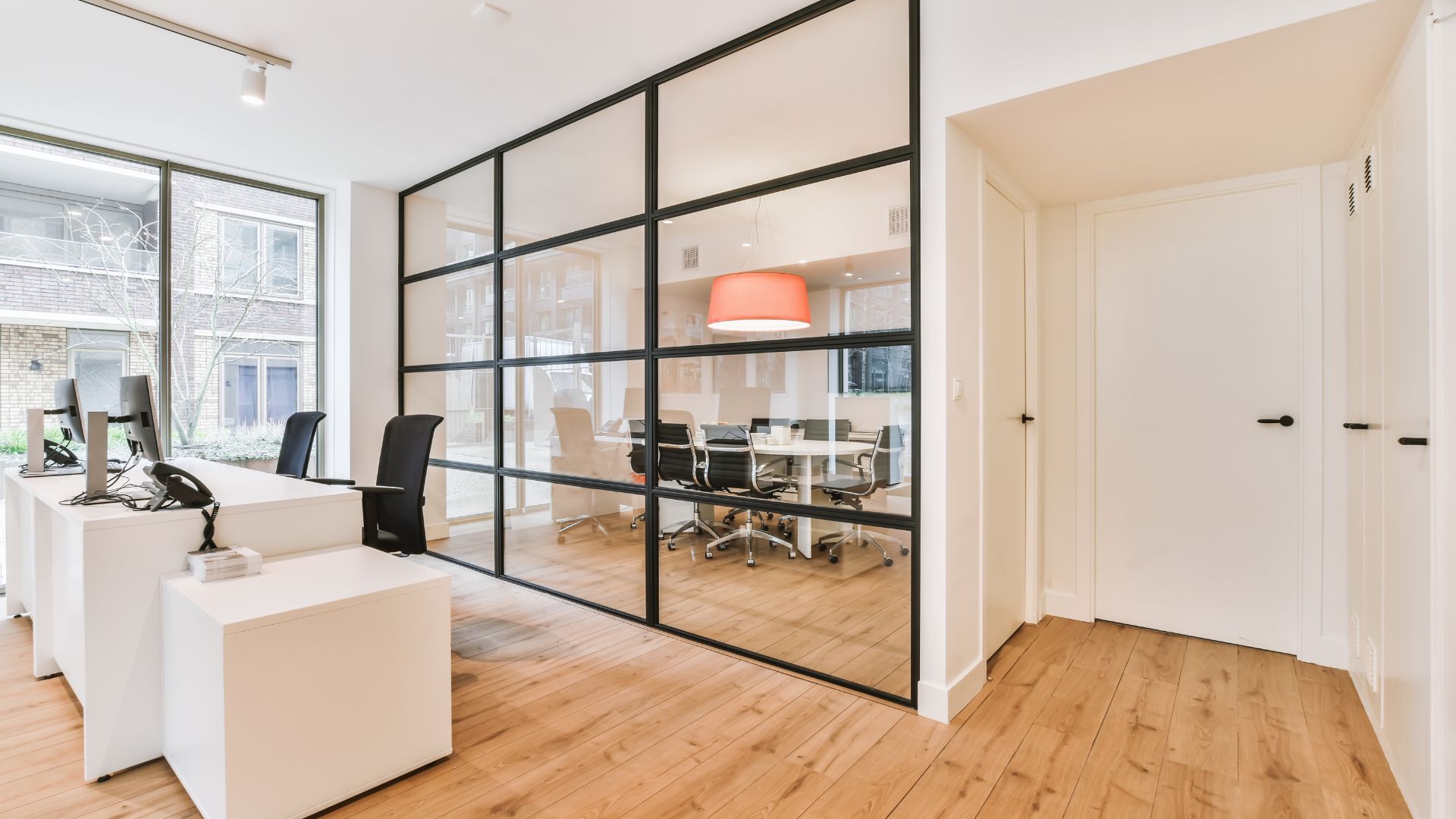 Modern office with glass partition, white desks, and wooden flooring