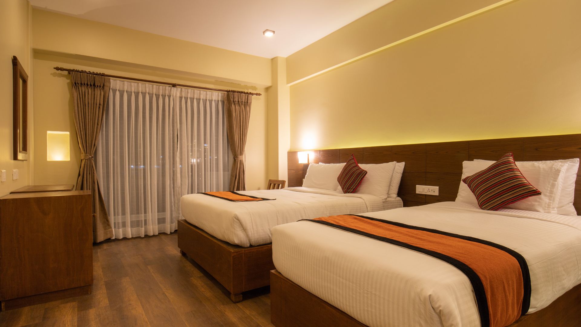 Cozy hotel room with two beds, warm lighting, and orange accents