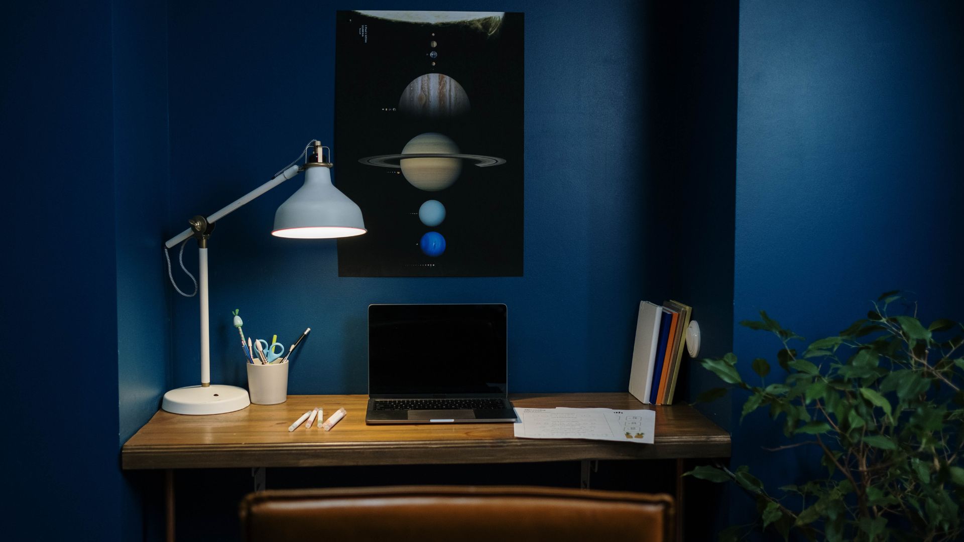 Home workspace with laptop, lamp, and planetary poster on blue wall